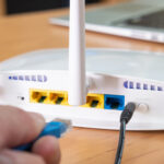 Selective focus at router antenna while men hand connecting fiber cable plug into socket with blurred computer laptop at the background. High speed broadband internet technology at home concept.